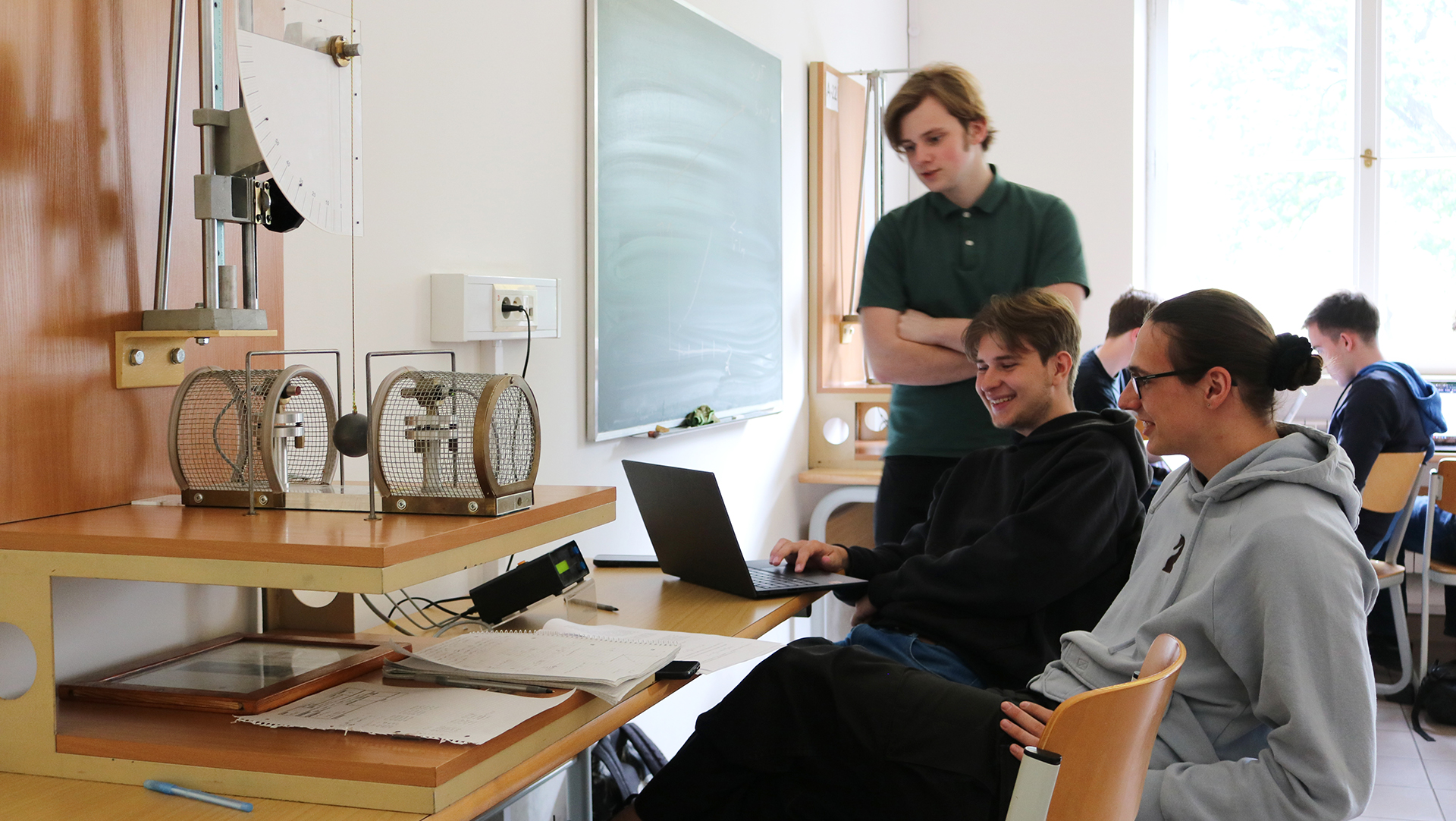 Grupa uśmiechniętych studentów patrząca na ekran laptopa w jednej z sal warsztatowych